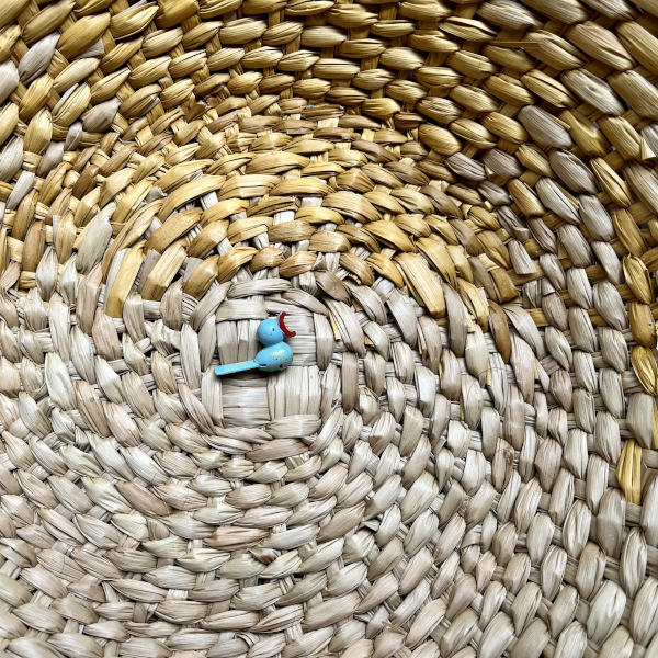 A tiny painted wooden bird displayed at the bottom of a basket.